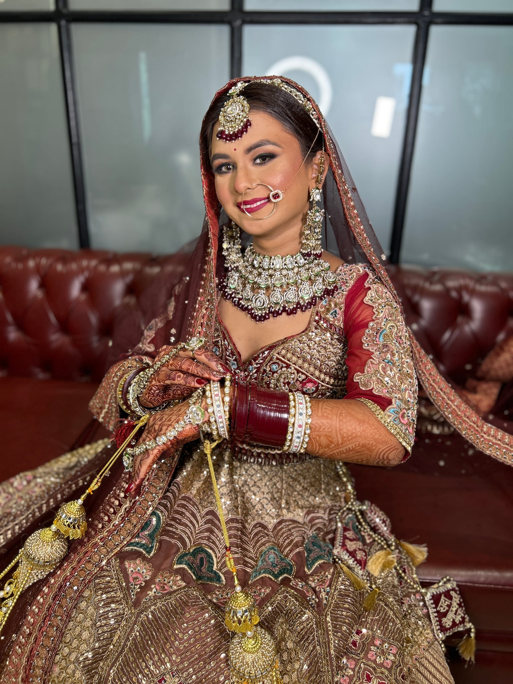 A bride seated in maroon and gold with her chooda and kaleere